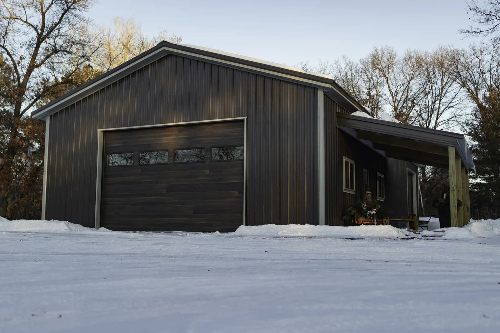 Custom Sherman pole barn garage with dark steel siding, wood-tone overhead door, and covered lean-to in a Minnesota winter setting