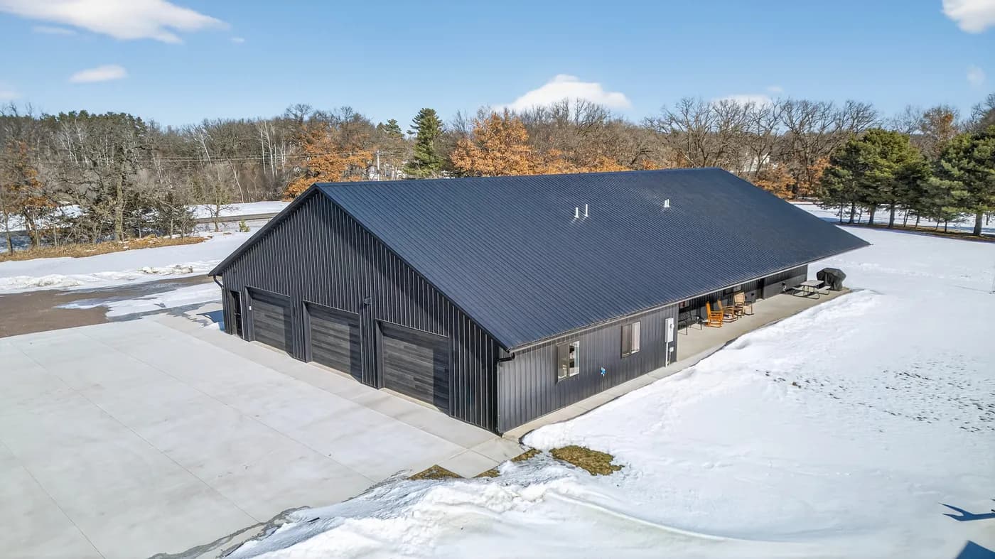 Connie House barndominium in Princeton with dark metal siding, three garage doors, and a covered porch in winter