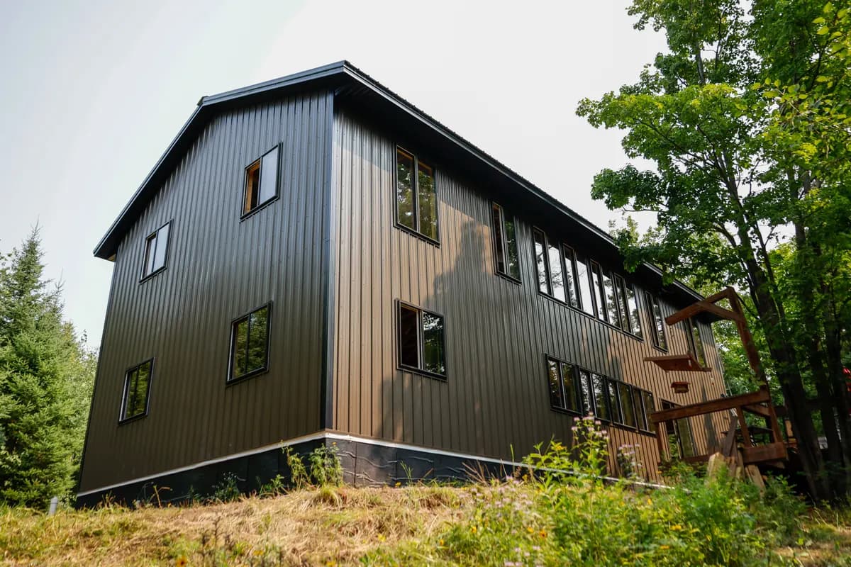 Tomsky two-story home exterior with metal siding and tall windows on a wooded property